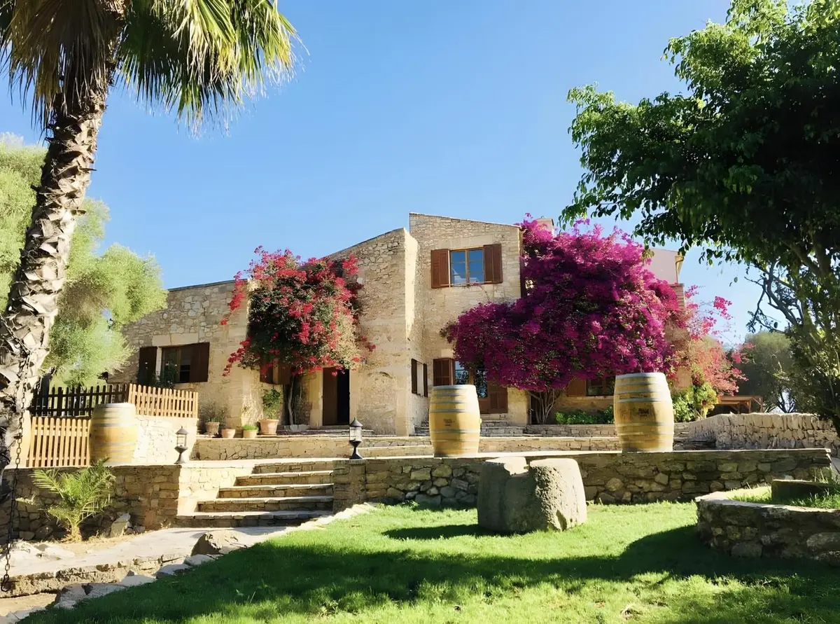 Natursteinfassade mit blühender Bougainvillea, davor Rasen und Terrassenstufen