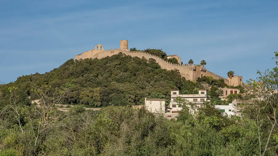 Das Castell de Capdepera mit seiner Zinnenmauer über dem bewaldeten Hügel, davor die Häuser des Ortes