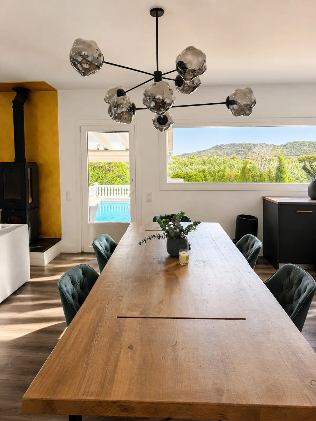 Essbereich mit langem Holztisch, Designleuchte und Blick zum Pool