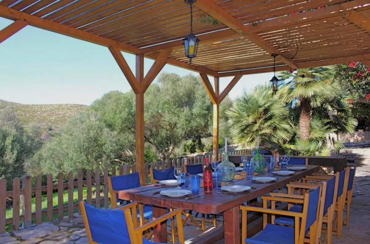 Langer Esstisch unter der Holzpergola mit Blick über Olivenbäume und Hügel
