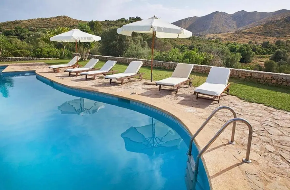 Pool mit Liegen und Sonnenschirmen, dahinter die Hügel der Serra de Llevant
