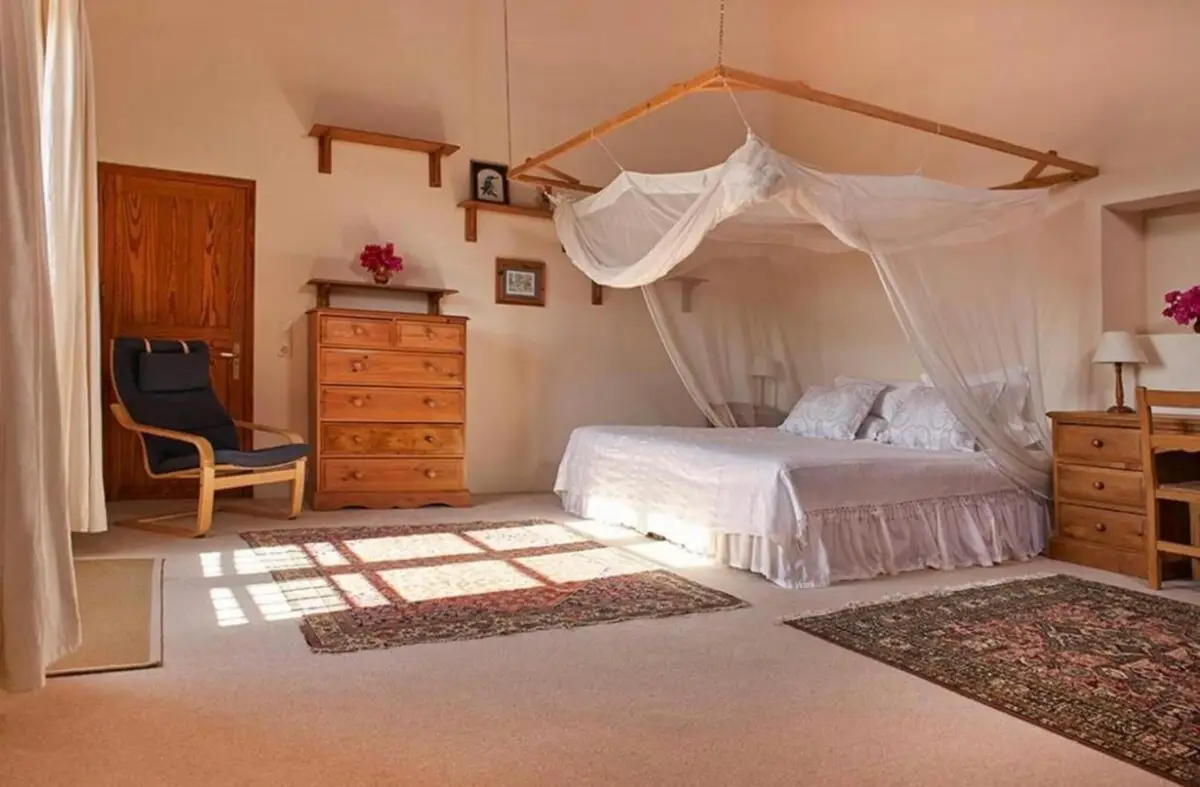 Schlafzimmer mit Himmelbett, Holzkommode und Sessel