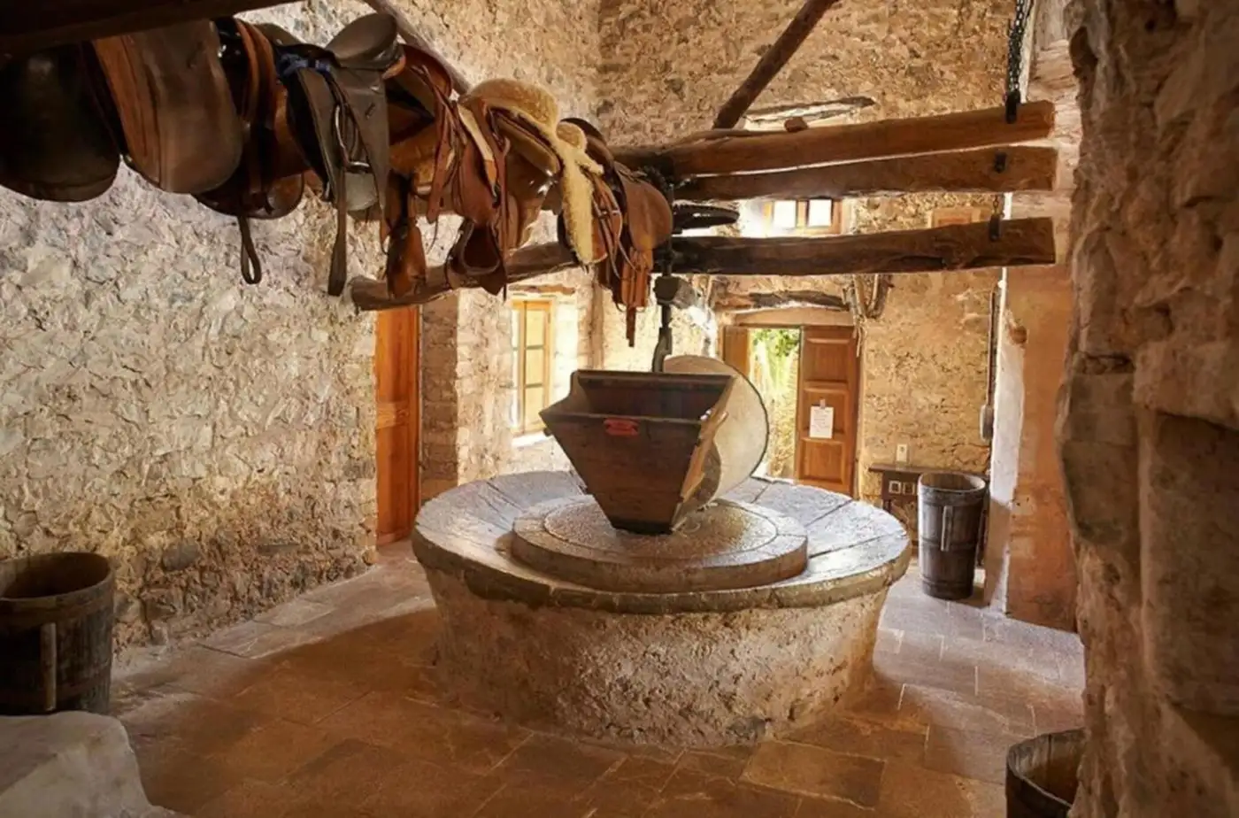 Mühlstein der historischen Tafona unter dem Deckenbalken, darüber hängende Sättel